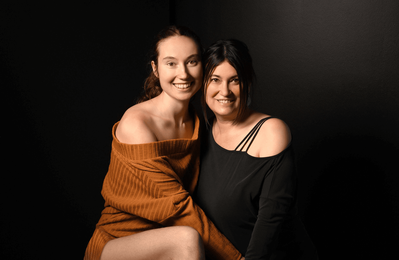 A smiling mother and daughter wearing comfortable black and orange off the shoulder sweaters at Kliks Photography.