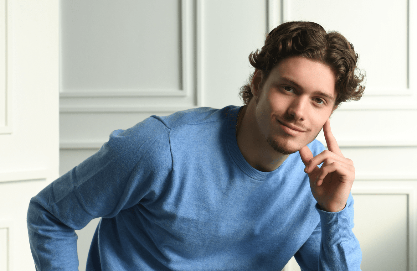 A boy in a blue sweater leans his chin in his hand during his senior photo session.