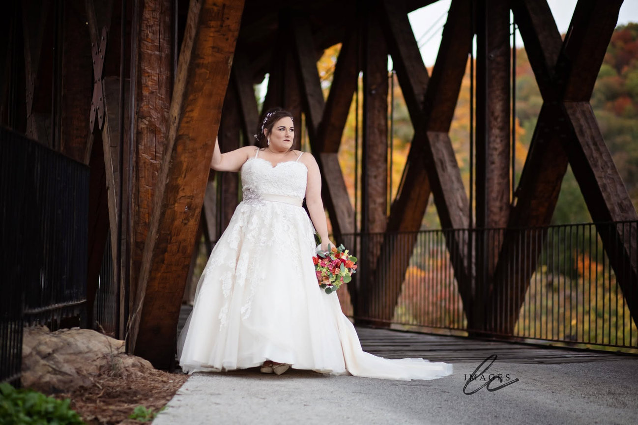 Bride in a white gown posing on a wooden bridge with a bouquet