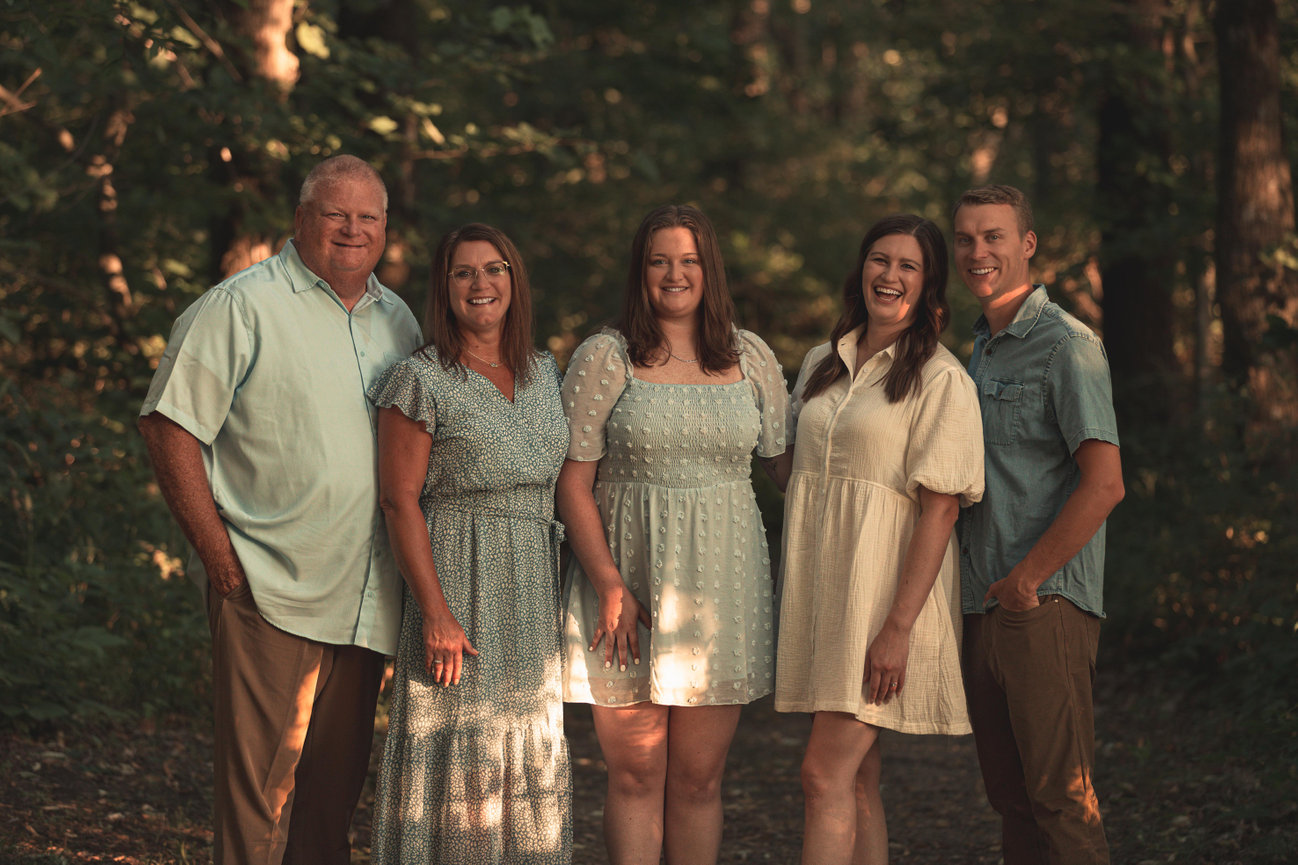 Family posing in a forest setting with dappled sunlight