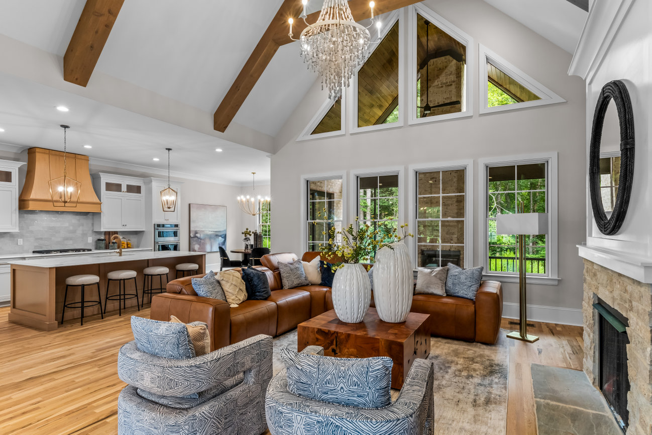Open-concept living room and kitchen with vaulted ceilings, leather sofa, fireplace, and large windows