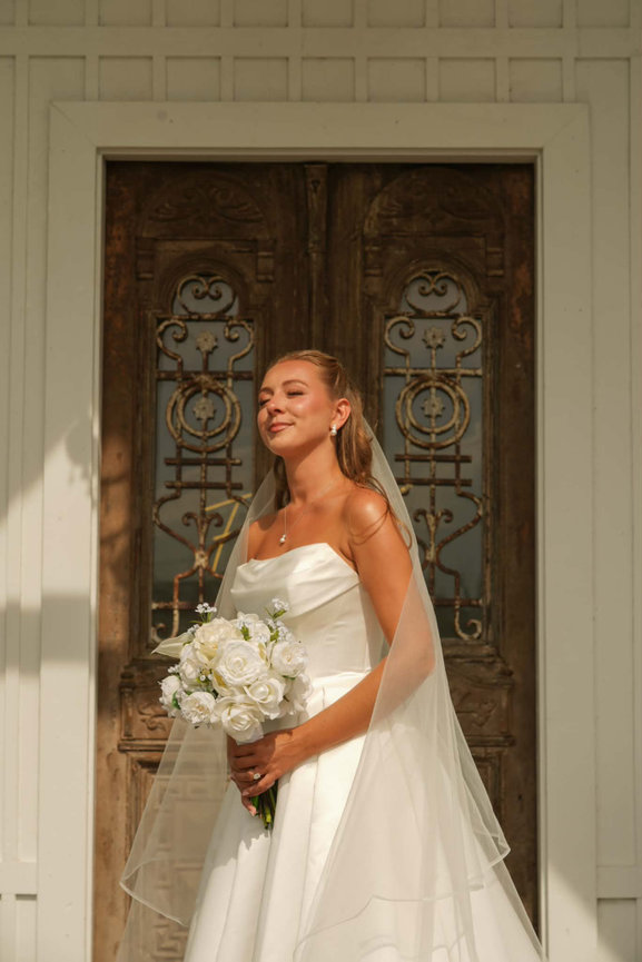 Bride holding a bouquet in front of a decorative doorway.