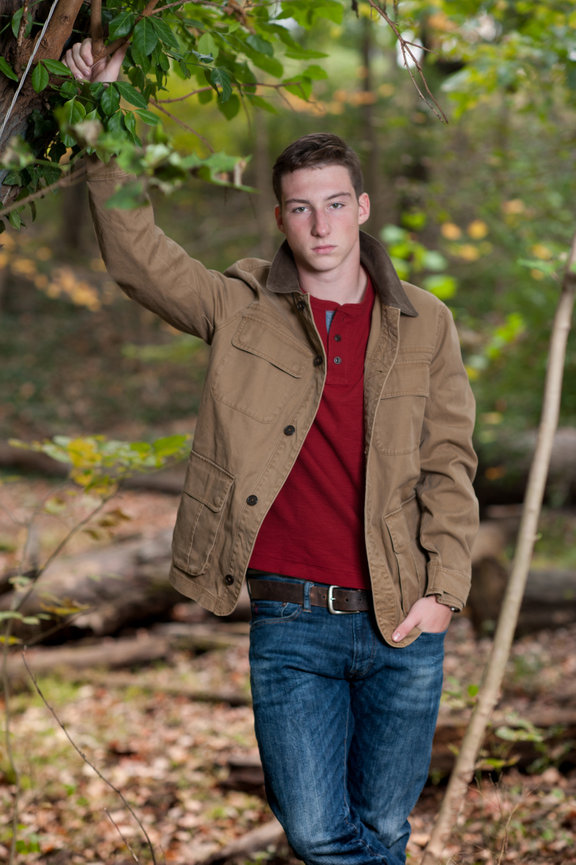 Teenage boy with a tan jacket and jeans leaning against a tree for senior photos in Dublin OH.