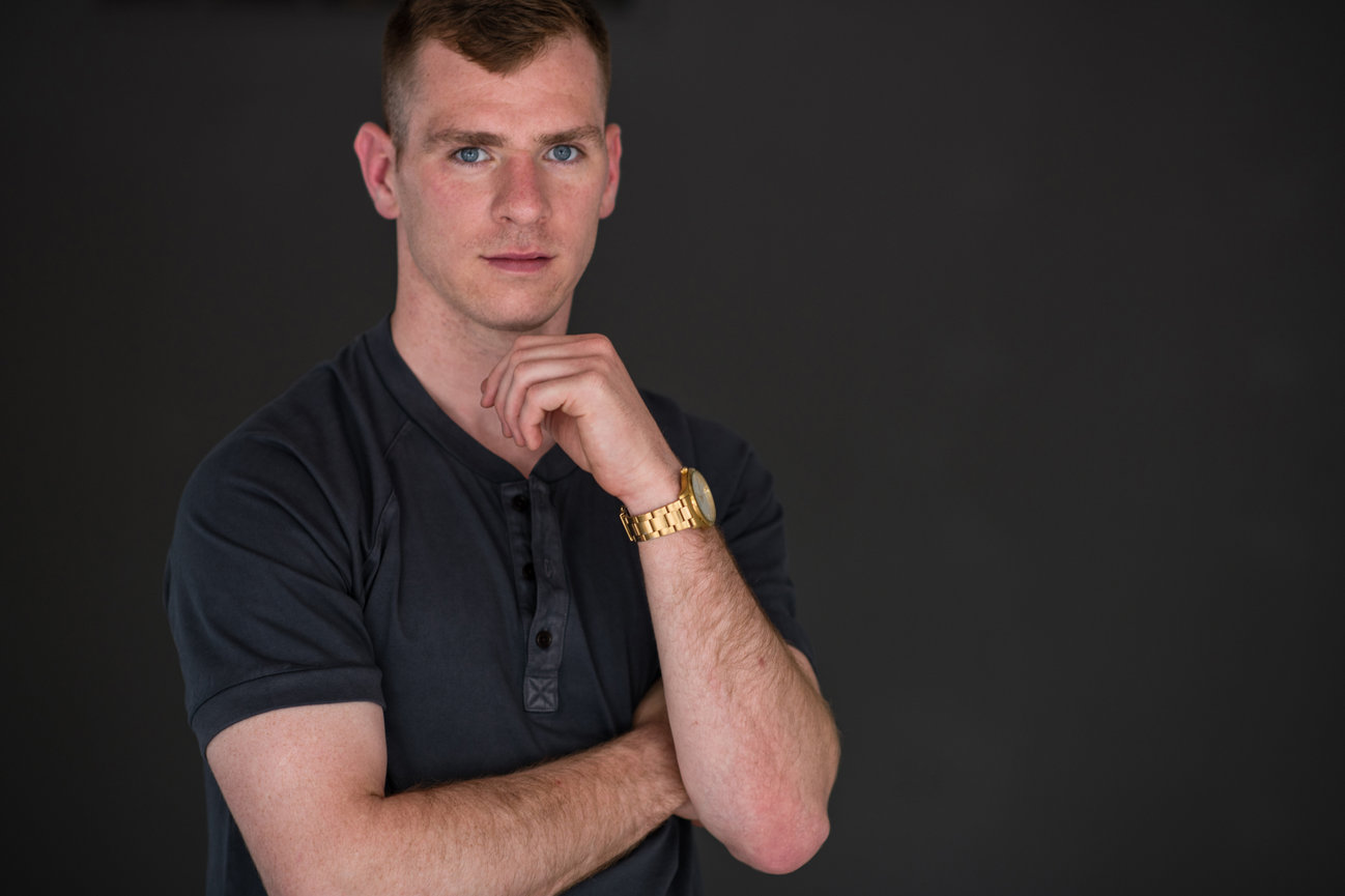 Man in a black shirt, looking confidently at the camera with a thoughtful expression, against a dark background, being photographed for updated business portraits in dublin ohio studio.