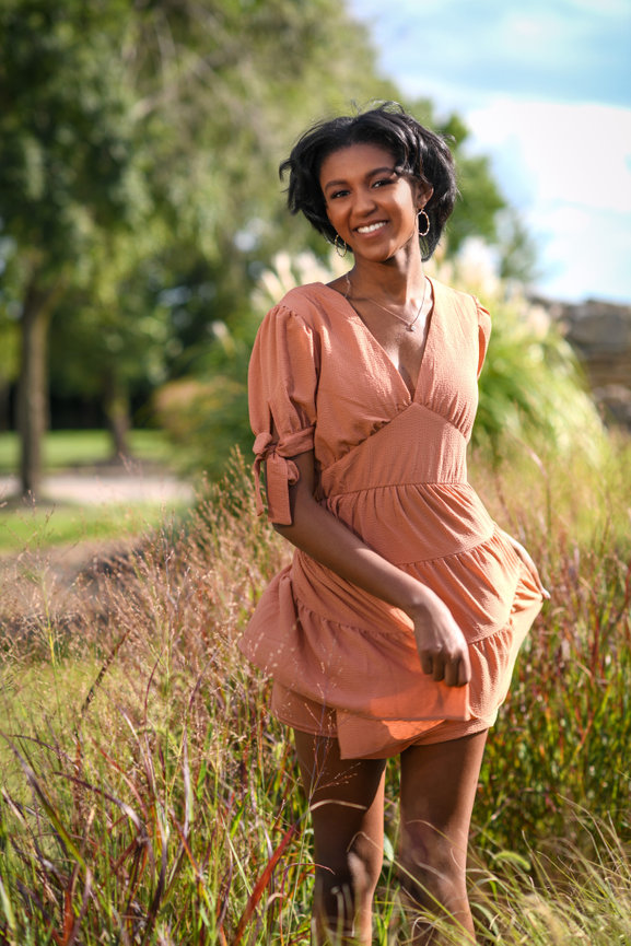 Gorgeous teen girl running through a field of tall grasses in a coral dress during her senior portrait session.