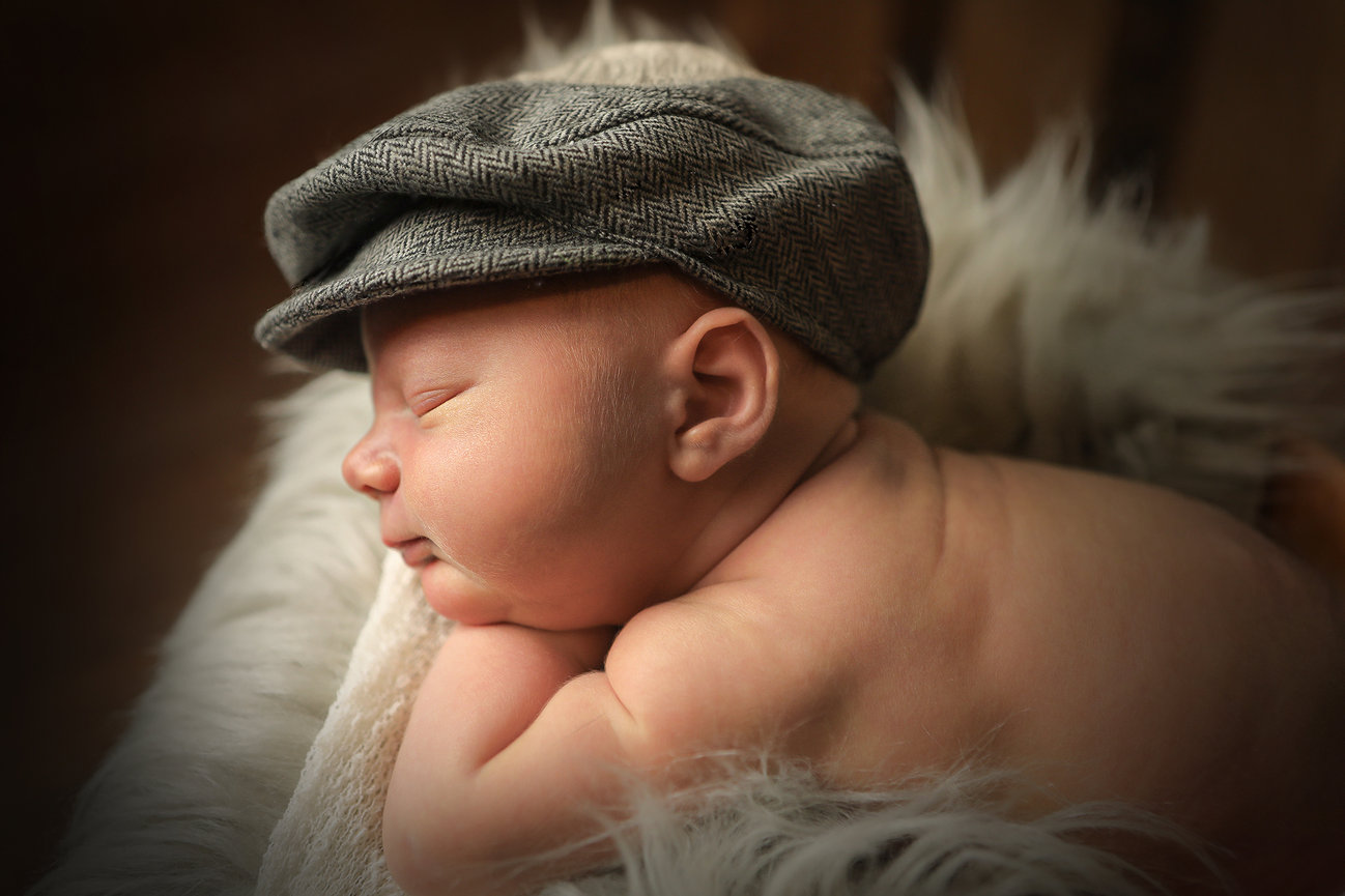 Sleeping baby wearing a grey cap, nestled on a fluffy white blanket.